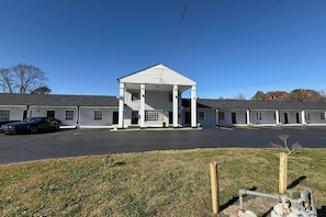 A motel with a central covered area, a parking lot, and a grassy foreground. - King Bed|Smoking|Danville VA (Danville VA)