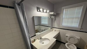 Une salle de bain avec un lavabo blanc, un miroir, des toilettes et une fenêtre avec des stores.