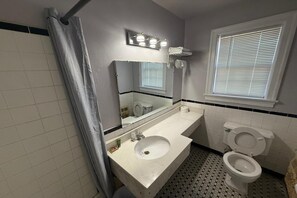 A bathroom with a white sink, a mirror, a toilet, and a window with blinds. - 2 Full Beds Non-Smoking (Danville VA)