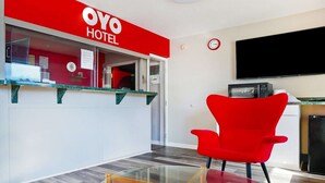 Un espace d’accueil d’hôtel aux couleurs rouge et blanche, avec un comptoir en verre, un fauteuil rouge, un téléviseur à écran plat et un four à micro-ondes.