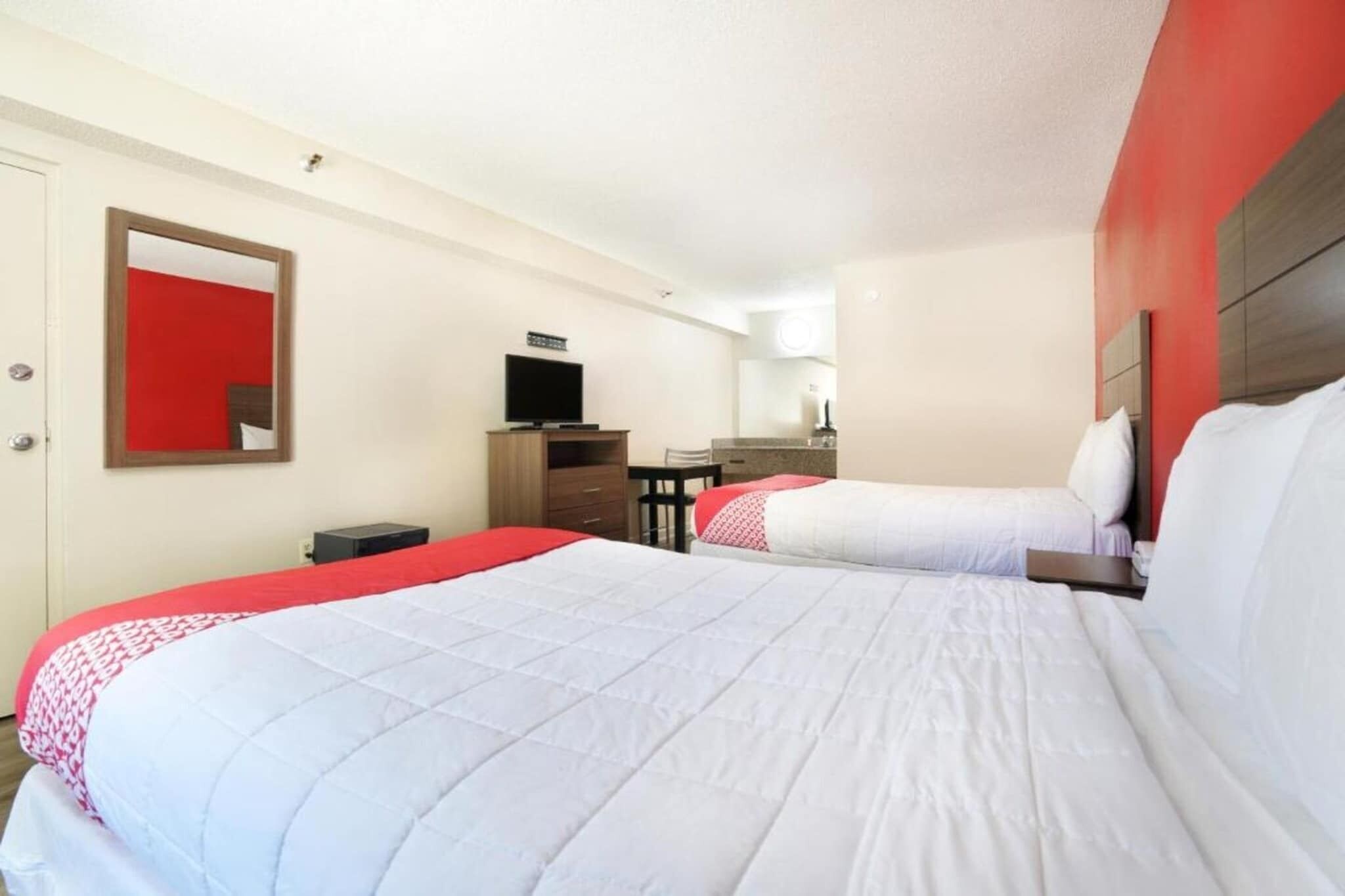 A hotel room with two beds, a TV, a desk, and a mirror.
