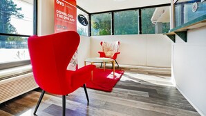 Une chambre d’hôtel moderne avec une grande fenêtre, un fauteuil rouge, une petite table ronde et un tapis rouge.