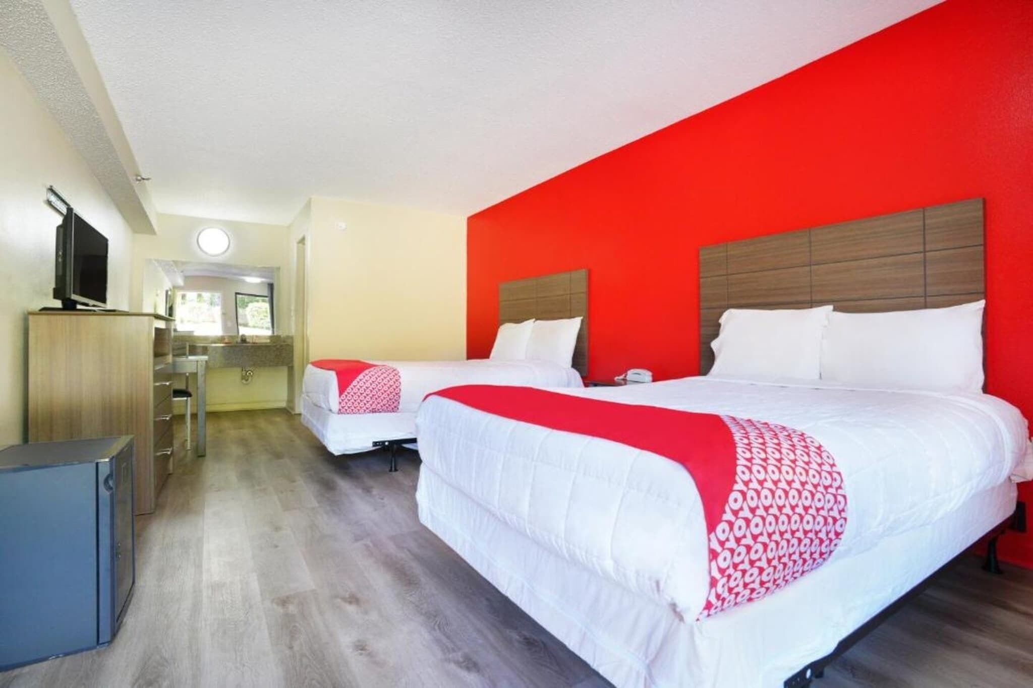 A hotel room with two beds, a TV, a desk, and a small kitchenette.