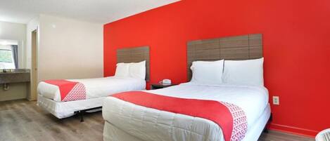 Habitación de hotel con dos camas, una pared de acento roja y suelo de madera.