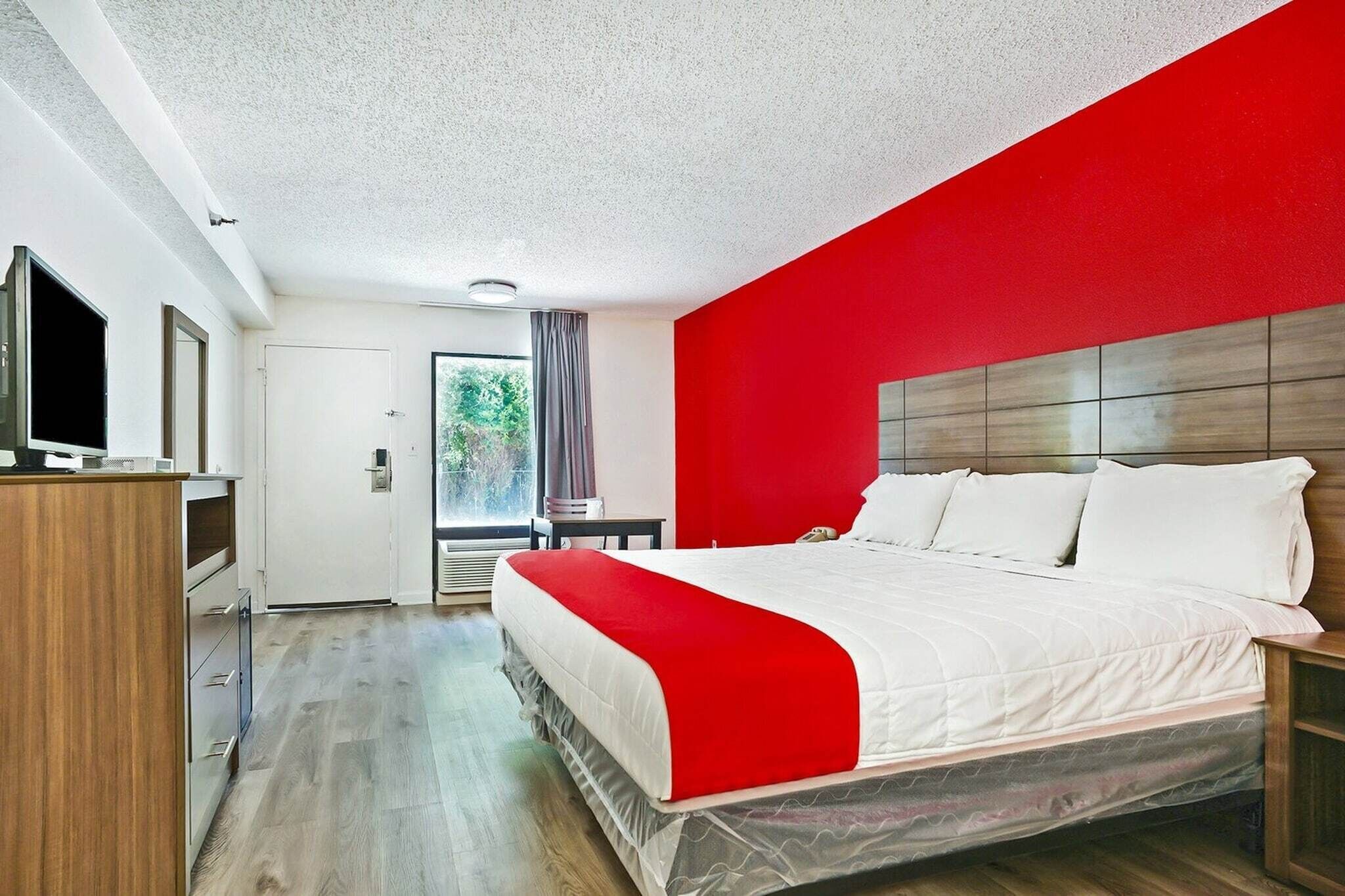 A hotel room with a bed, a TV, a desk, and a window with curtains.