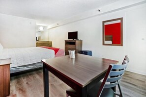 Ett hotellrum med en säng, ett träbord, en stol, en tv, en byrå och en spegel.