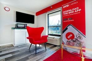 Una habitación de hotel moderna con una silla roja, un televisor de pantalla plana, un microondas y un ventanal grande.