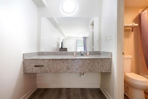 Un baño con lavamanos de encimera de granito, espejo, inodoro y cortina de ducha.