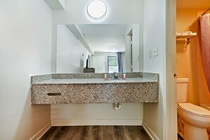 Ein Badezimmer mit Marmorwaschtisch, Spiegel, Toilette und Duschvorhang.