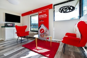 A modern hotel room with a red accent wall, a flat-screen TV, a microwave, a glass table, and two red chairs. - Decatur GA | King Bed (Decatur GA)