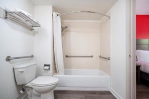A bathroom with a toilet, shower, and bathtub, equipped with grab bars and a towel rack. - Decatur GA | King Bed (Decatur GA)