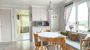 A kitchen with white cabinets, a microwave, and a refrigerator. There is a dining table with chairs and a window with curtains. - Apartment Near the Sea in Skärhamn | SE09178 (Skärhamn)