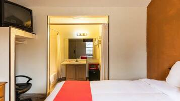 A hotel room with a bed, a desk, a chair, a television, a mirror, a sink, and a microwave.