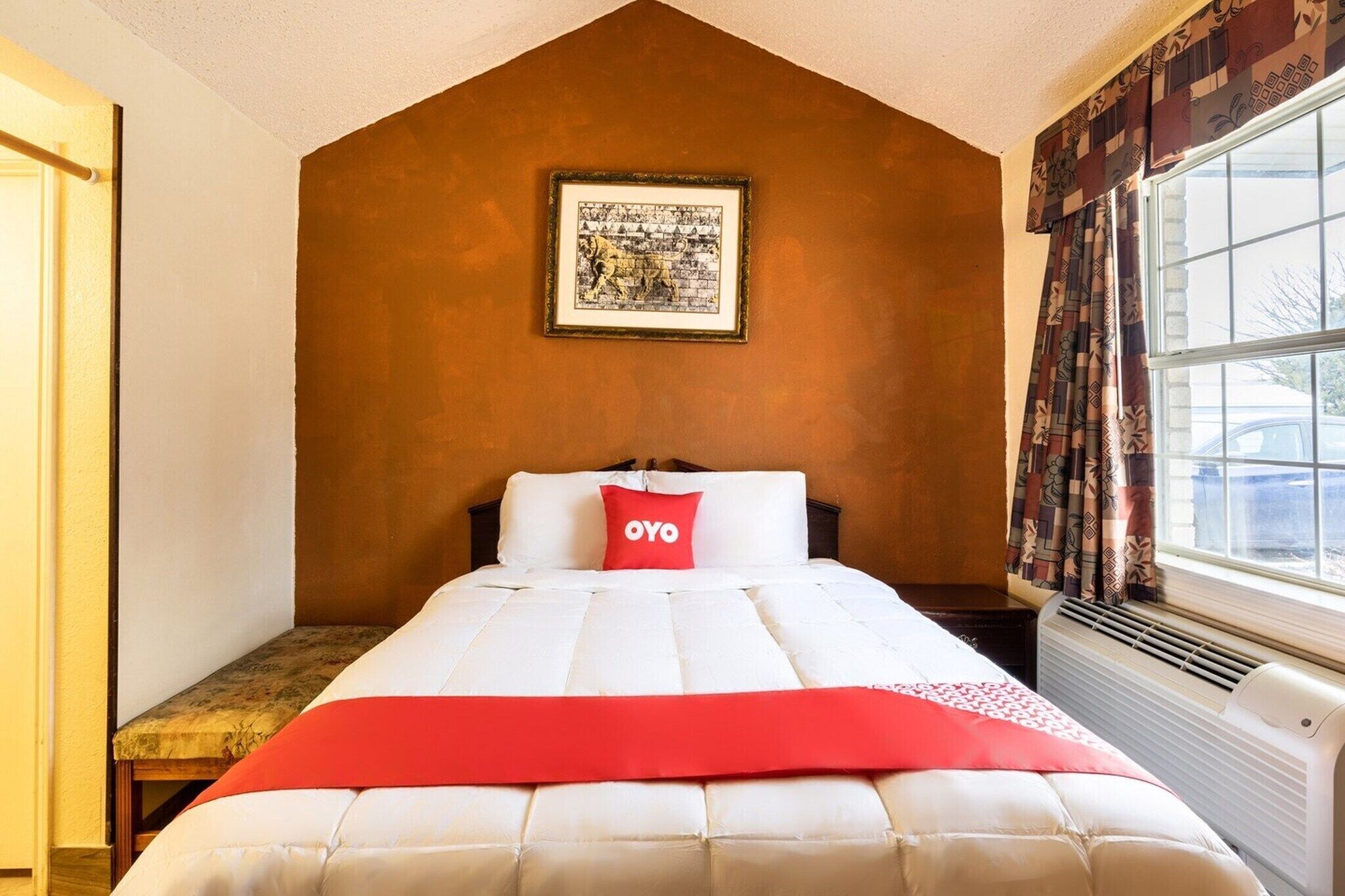 Un dormitorio con cama, un cuadro en la pared, una ventana con cortinas y una mesita de noche.