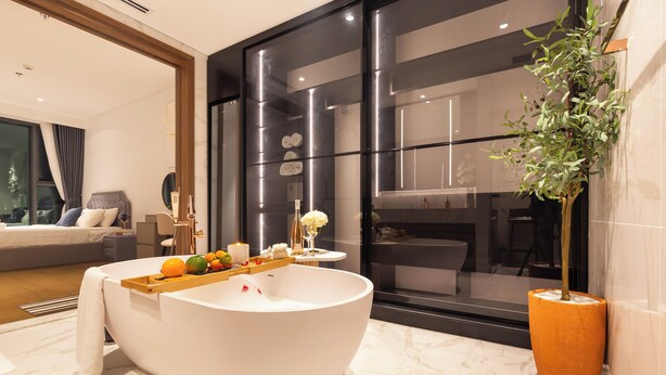Ein modernes Badezimmer mit einer großen, ovalen Badewanne, einem Holztablett mit Früchten und einer Kerze sowie einem Blumentopf.