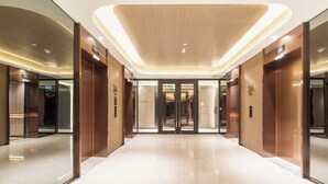 Eine moderne Hotelhalle mit glänzendem Boden, Holzvertäfelung an den Wänden und einem Glasaufzug.