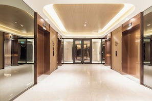 Eine moderne Hotelhalle mit glänzendem Boden, Holzvertäfelung an den Wänden und einem Glasaufzug.