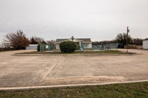 A large, empty parking lot with a gated entrance, a small building, and a fenced area.