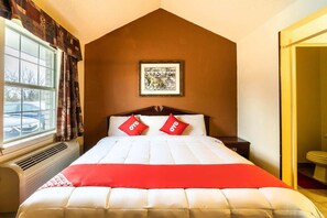 A hotel room with a large bed, a window with curtains, a framed picture on the wall, and a door leading to a bathroom.