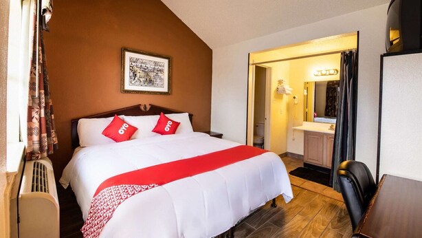 Ein Hotelzimmer mit einem Bett, einem gerahmten Bild an der Wand, einem Badezimmer mit Spiegel und einem Sessel.