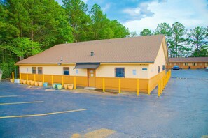 A motel with a single-story structure, a parking lot, and a row of motel rooms in the background.