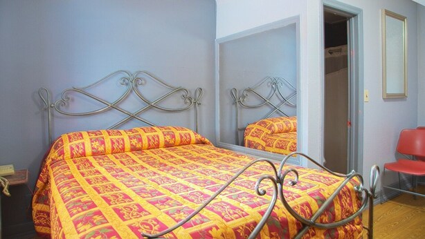 A bedroom with a metal bed frame, a patterned bedspread, a mirror, and a red chair.