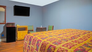 A bedroom with a bed, a small table, a chair, a TV, and a microwave.