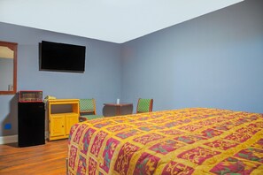 Un dormitorio con una cama, una mesita, una silla, un televisor y un microondas.