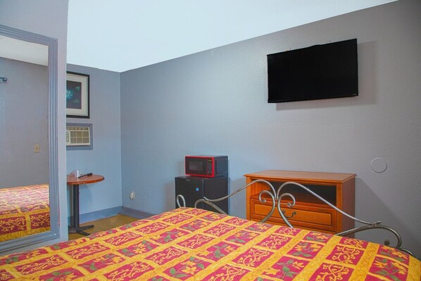 A bedroom with a bed, a dresser, a microwave, and a television on the wall.