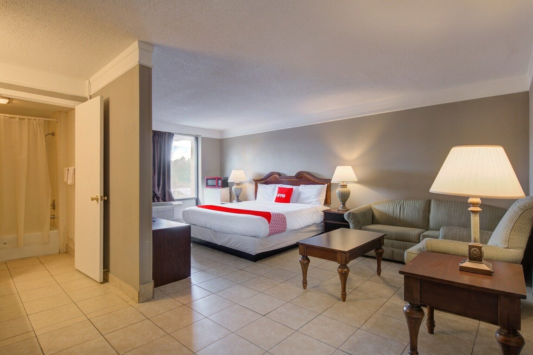 A hotel room with a bed, a sofa, a coffee table, and a lamp.. Douglas GA|Queen Bed