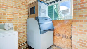 A compact room with a brick wall, a window, a built-in washer and dryer, and a sign indicating guest laundry room availability. - Douglas GA|Queen Bed (Douglas GA)