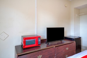 Una habitación con un aparador de madera, un microondas rojo y un televisor negro.