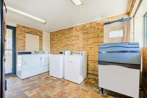 A laundry room with a brick wall, a sign indicating guest laundry closing at 9:00 PM, and a white door.