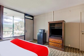 A hotel room with a bed, a television, a minibar, and a sliding glass door to the outside. - Douglas GA | King Bed (Douglas GA)