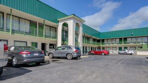 Ein Motel mit grüner Fassade, mehreren Parkplätzen und einem Eingang mit kleinem Bogen.