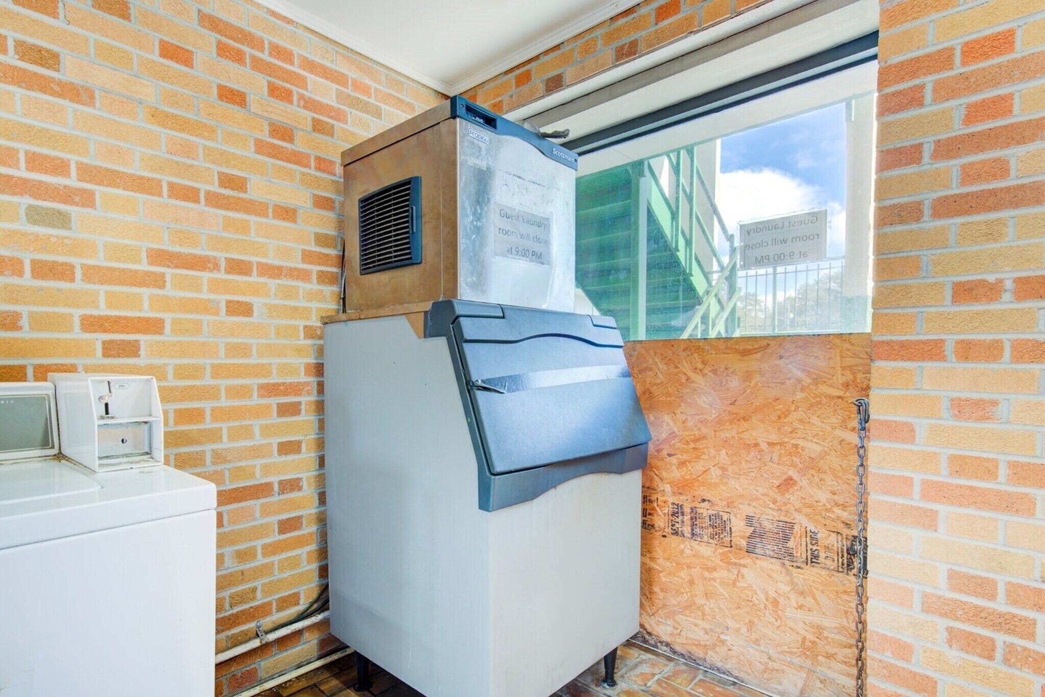 A compact room with a brick wall, a window, a built-in washer and dryer, and a sign indicating guest laundry room availability.