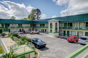 A motel with a central courtyard, multiple rooms with green accents, and a parking lot with several cars. - Premium 2 Queen Bed|Douglas GA (Douglas GA)