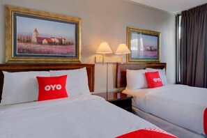 A hotel room with two beds, each with a red OYO pillow, two wall-mounted lamps, and two framed landscape paintings. - Premium 2 Queen Bed|Douglas GA (Douglas GA)