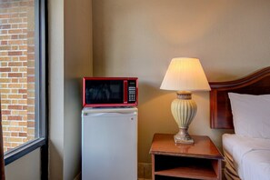 A hotel room with a microwave on a mini-fridge, a bedside lamp, and a bed.