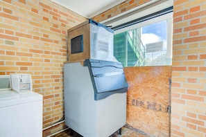 A compact room with a brick wall, a window, a built-in washer and dryer, and a sign indicating guest laundry room availability.