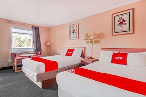 Habitació d'hotel amb dos llits, una escriptori, una cadira, una làmpada i una finestra amb cortines.