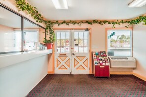 A room with a double door, a window with blinds, a vending machine, and a potted plant.