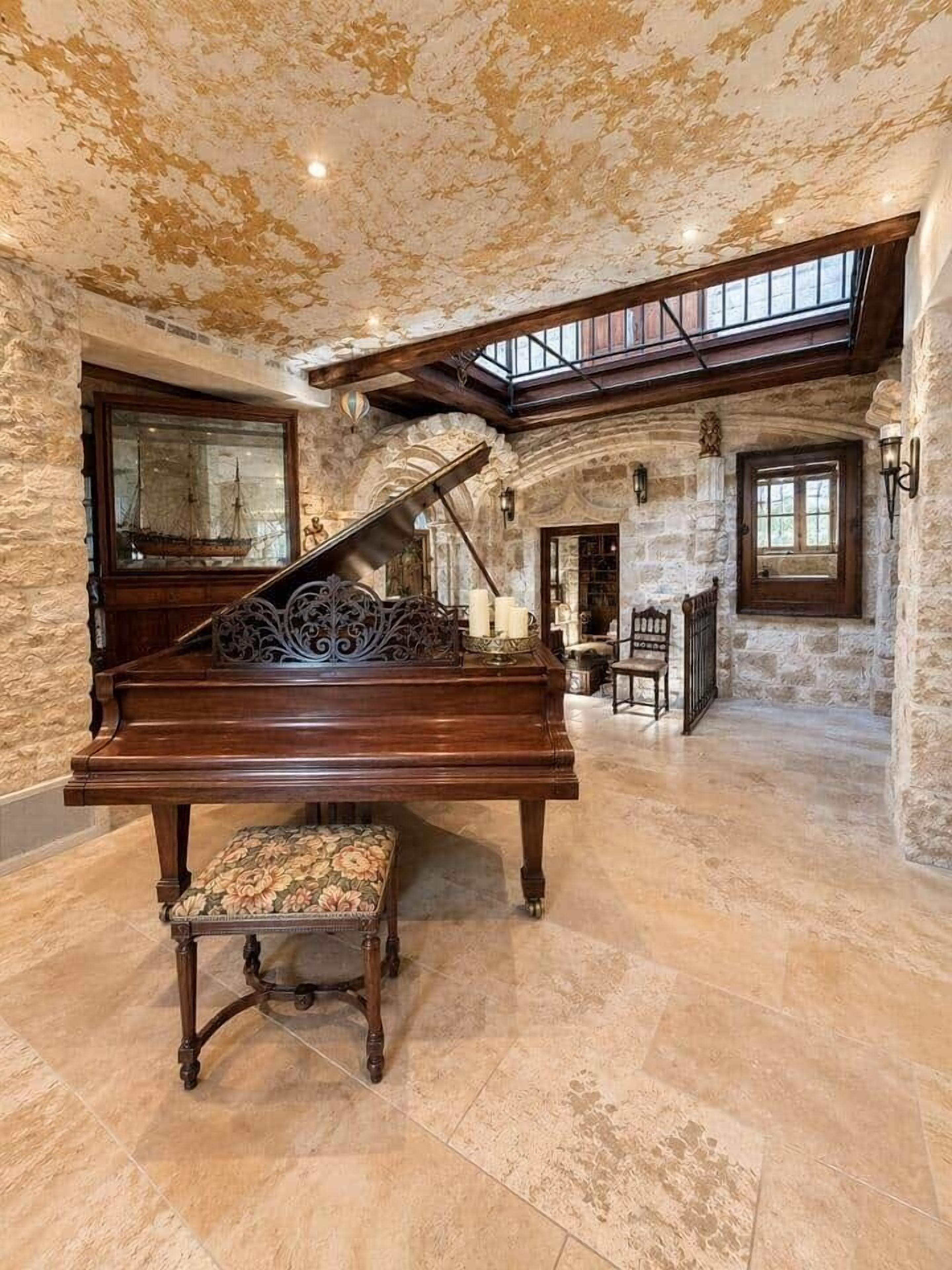 A grand piano in a spacious room with stone walls, a high ceiling, and a skylight.