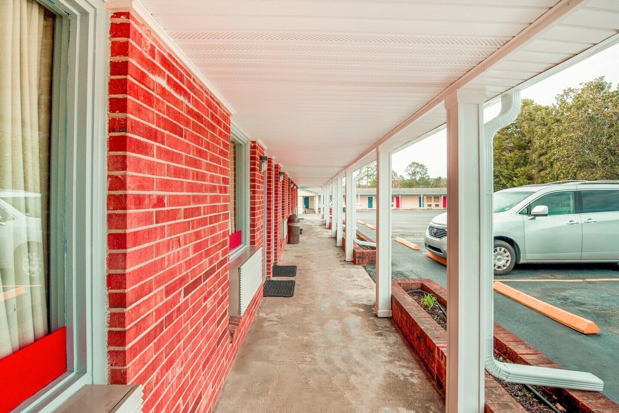 Un pasillo cubierto con una pared de ladrillo rojo, un coche estacionado afuera y un edificio con techo blanco.