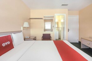 Een hotelkamer met een bed, nachtkastje, stoel, bureau en een deur naar de badkamer.