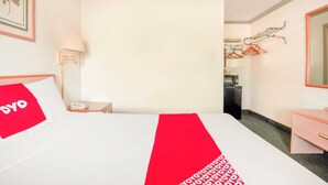 A hotel room with a bed, a bedside table, a lamp, a dresser, and a mirror.