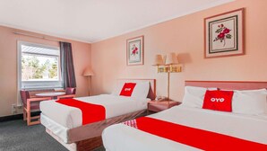 A hotel room with two beds, a desk, a chair, a lamp, and a window with curtains.