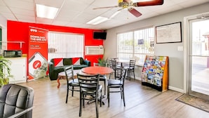 A hotel room with a red accent wall, a ceiling fan, a dining area with a round table and chairs, a sofa, a TV, and a window with blinds. - Texarkana TX | 2 Full Bed (Texarkana TX)