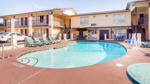 A hotel with a swimming pool, outdoor seating, and a two-story building.