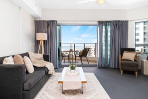 A modern living room with a sofa, armchair, coffee table, and a view of the balcony with a table and chairs. - Ocean Skyline Retreat | Infinity Pool, Gym & CBD (Darwin City)